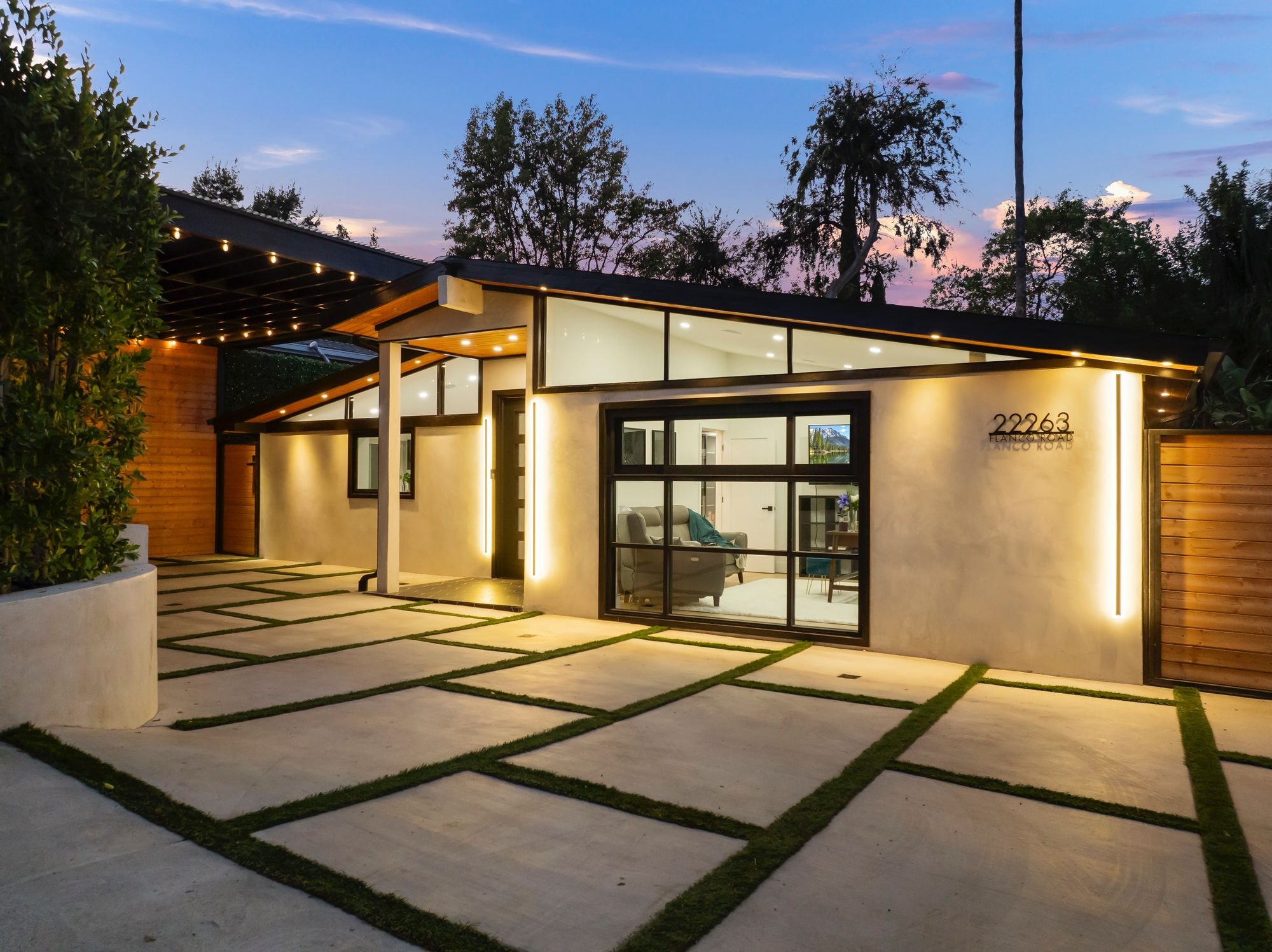 22263 Flanco Rd at twilight: mid-century modern facade glowing with warm interior light, string lights across the front courtyard, clerestory windows wrapping the great room.